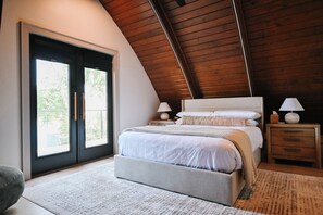 A bedroom with a large bed, two bedside tables with lamps, a wooden ceiling, and a sliding glass door leading to an outdoor area. - Acorn Cove by LittleCreek+Co, Waterfront + Private Dock + Air Hockey (Frankston)