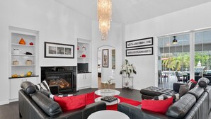 A modern living room with a fireplace, black leather sofas, a chandelier, and a large window with a view. - Oasis: Spacious 4BR Pool Home in Inverness (Inverness)