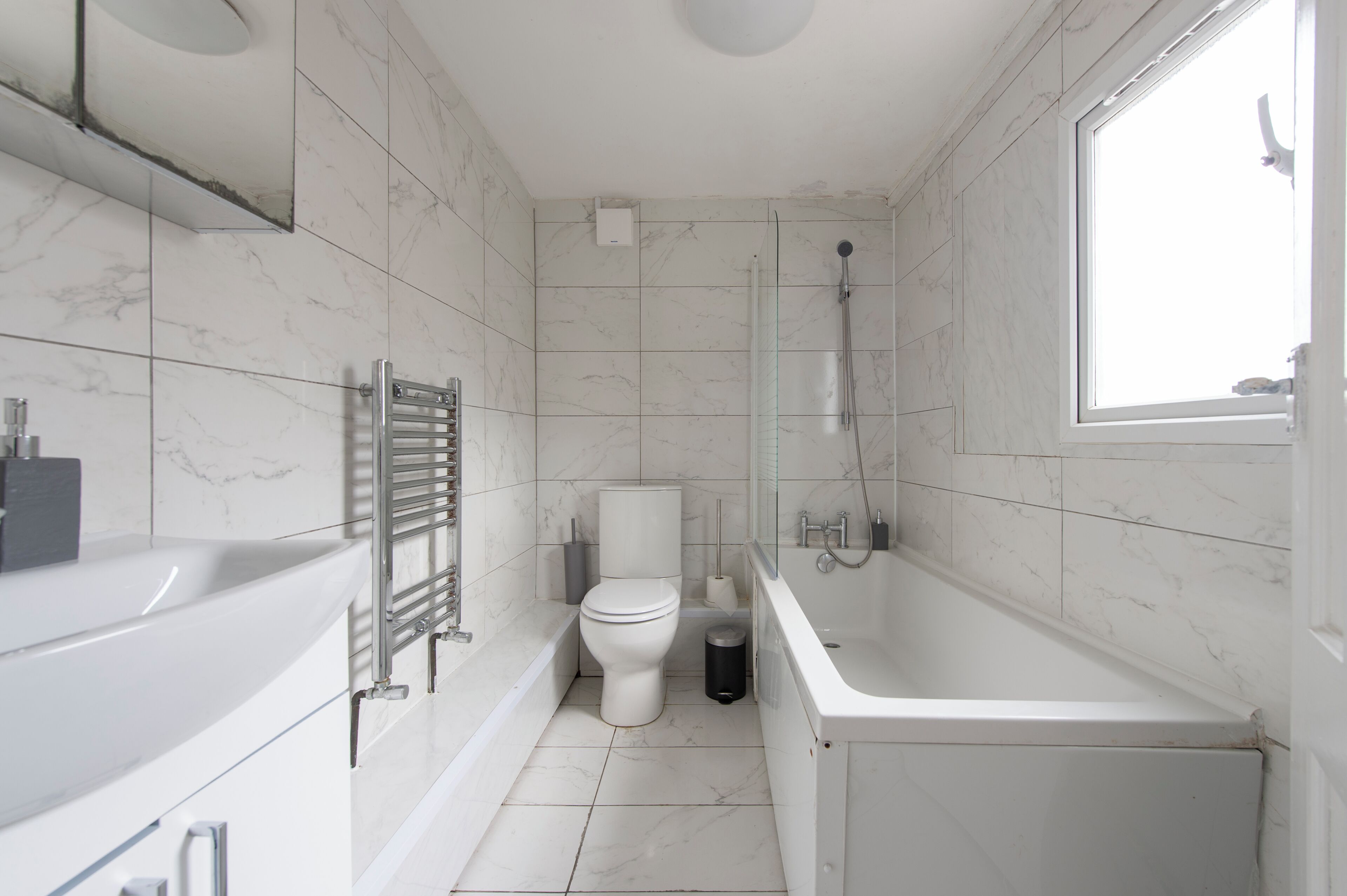 A modern bathroom with a bathtub, toilet, and shower area, featuring marble tiles and a large window.