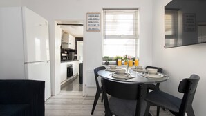 A modern kitchen with white appliances, a dining table set with plates, bowls, and glasses, and a sign on the wall. - Stylish 4BR Home WiFi FreeParking (Thornton Heath)
