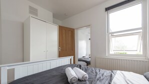 A bedroom with a bed, a wardrobe, a window, and a door leading to another room. - Stylish 4BR Home WiFi FreeParking (Thornton Heath)