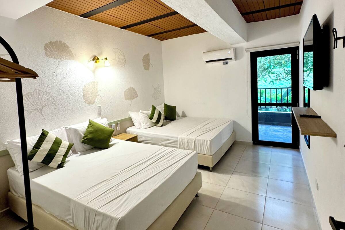 A bedroom with two beds, a wooden ceiling, a wall-mounted TV, and a door leading outside.