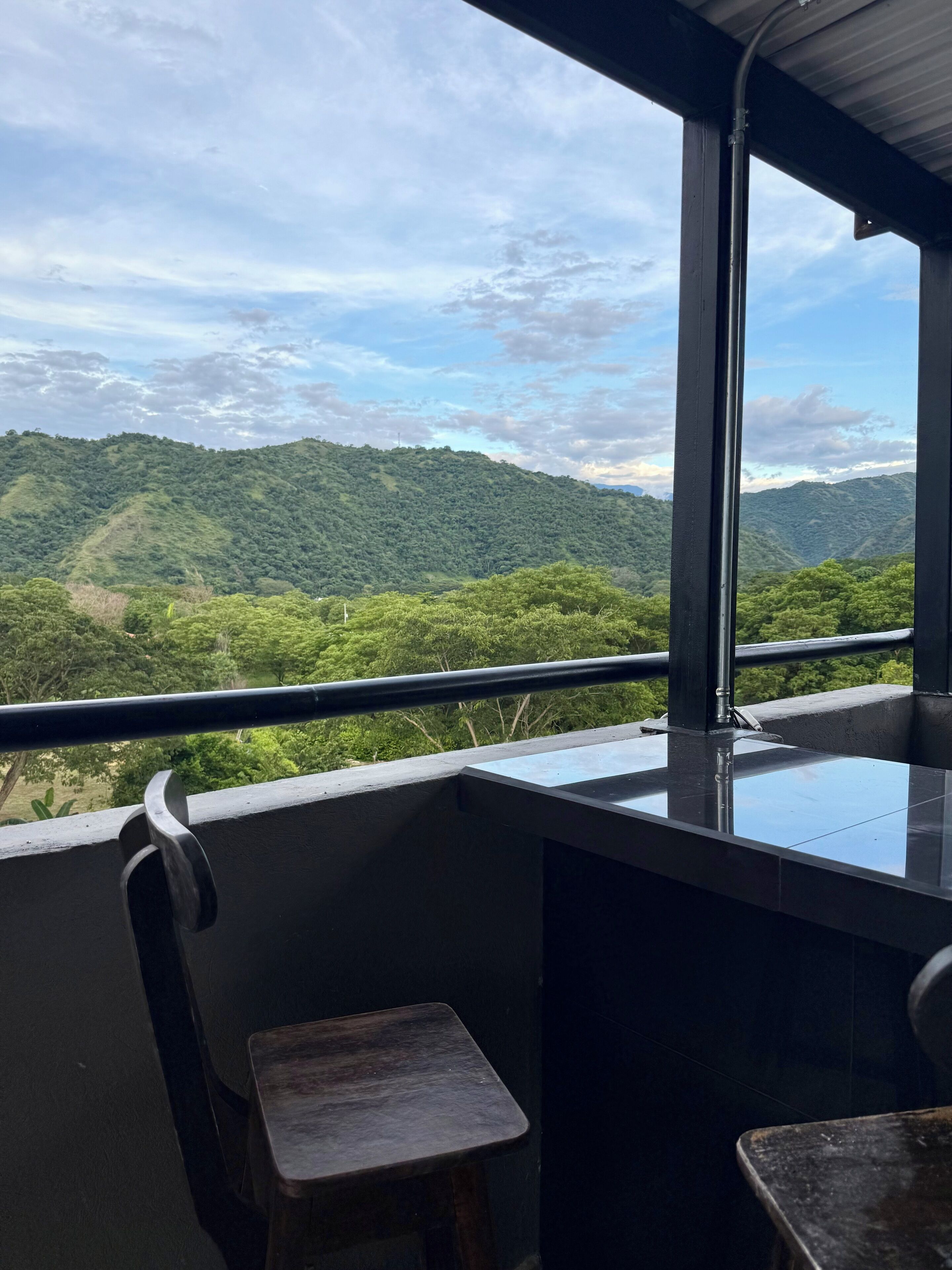 A balcony with a view of green hills and a cloudy sky.
