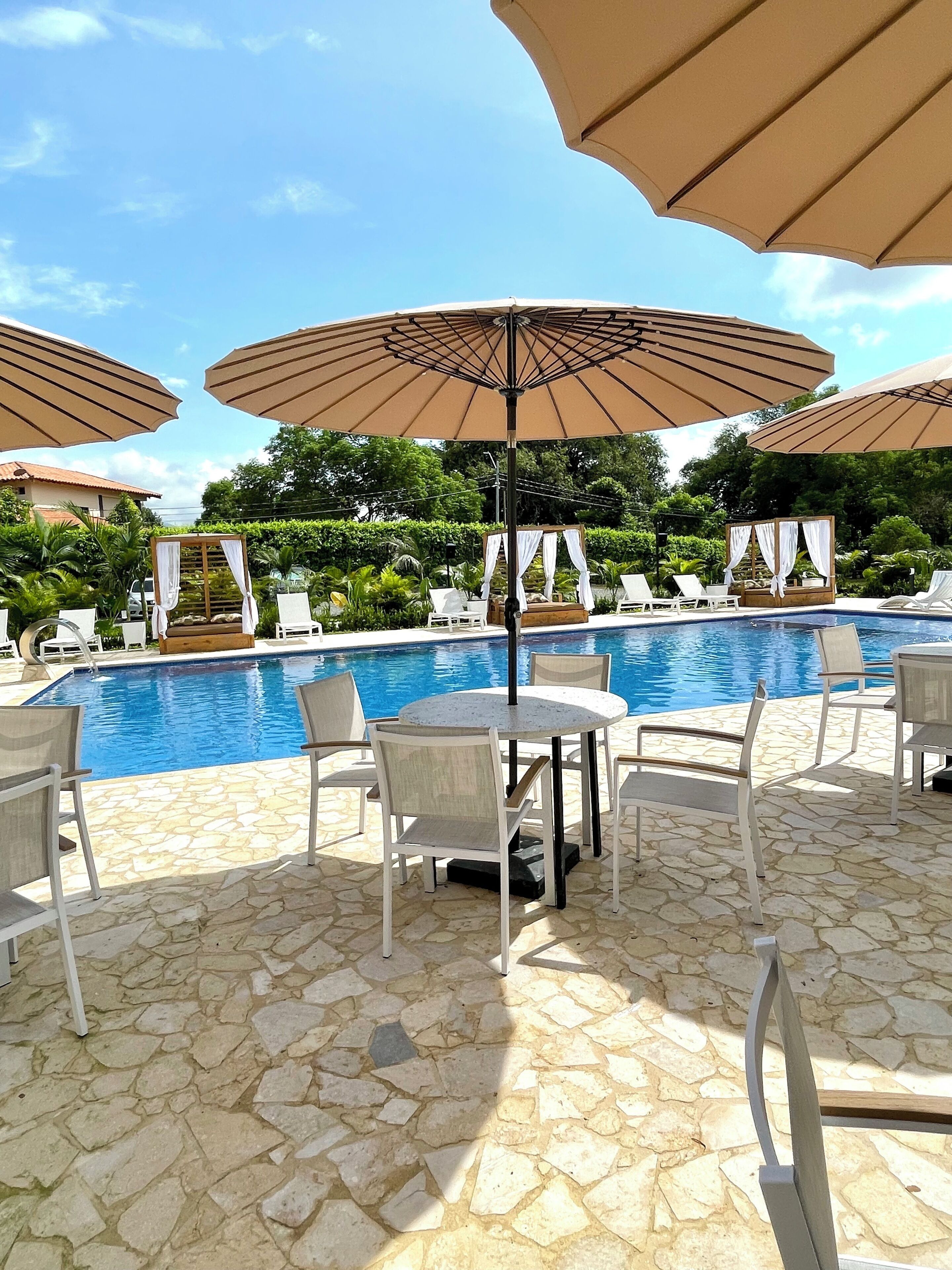 A poolside area with lounge chairs and umbrellas, a stone-tiled floor, and a clear blue pool.