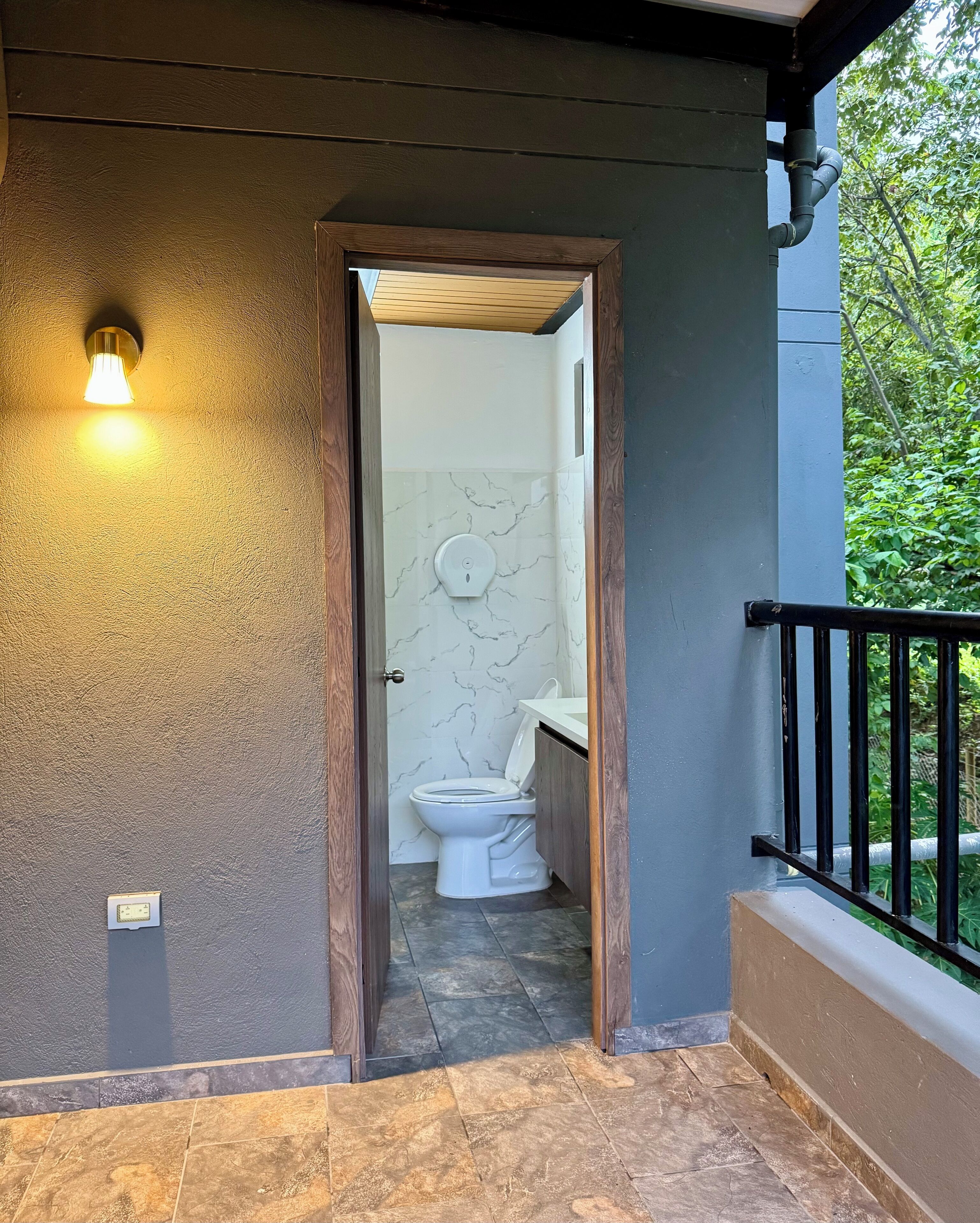 Une salle de bain avec des toilettes blanches, des murs en marbre et un cadre de porte en bois.
