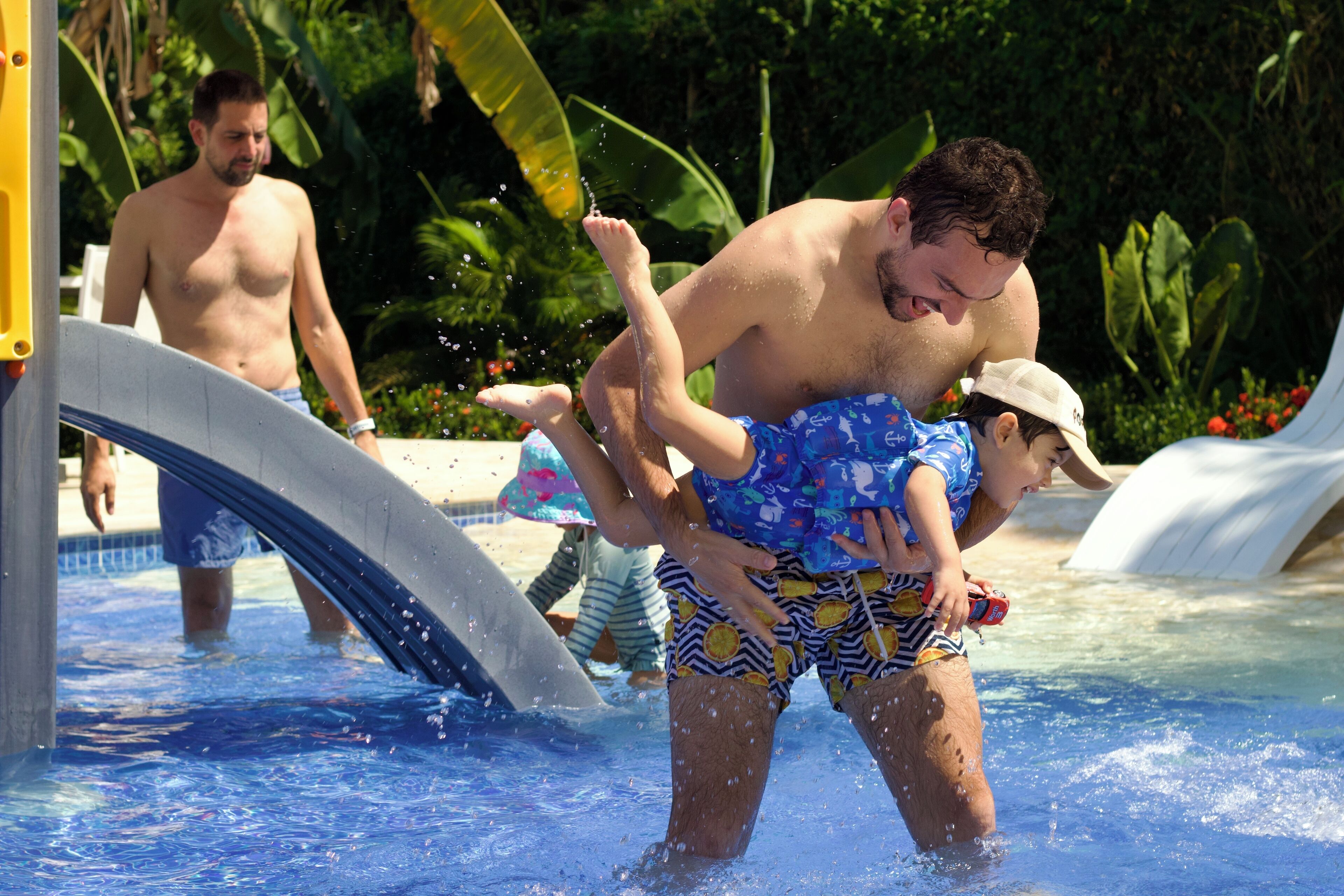 A swimming pool with a water slide and a man lifting a child.