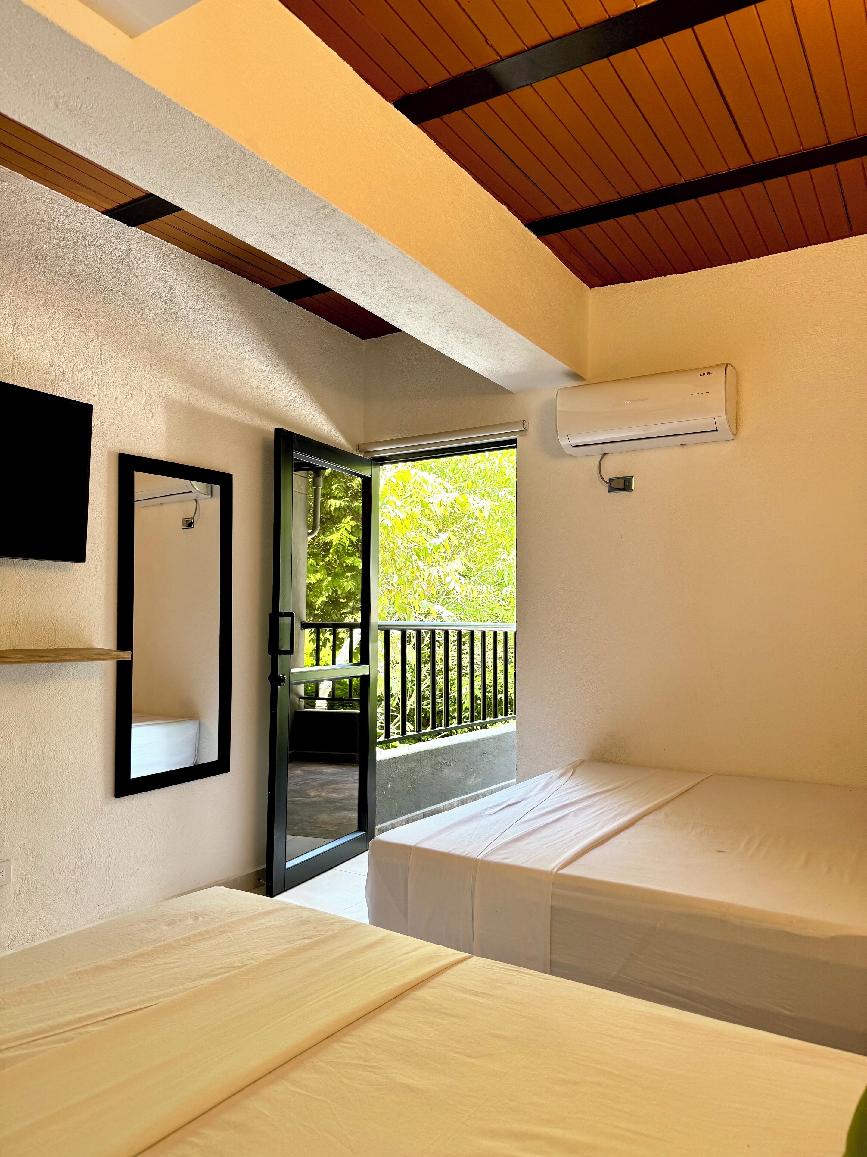 Una habitación con cama, espejo, aire acondicionado y balcón con barandilla.