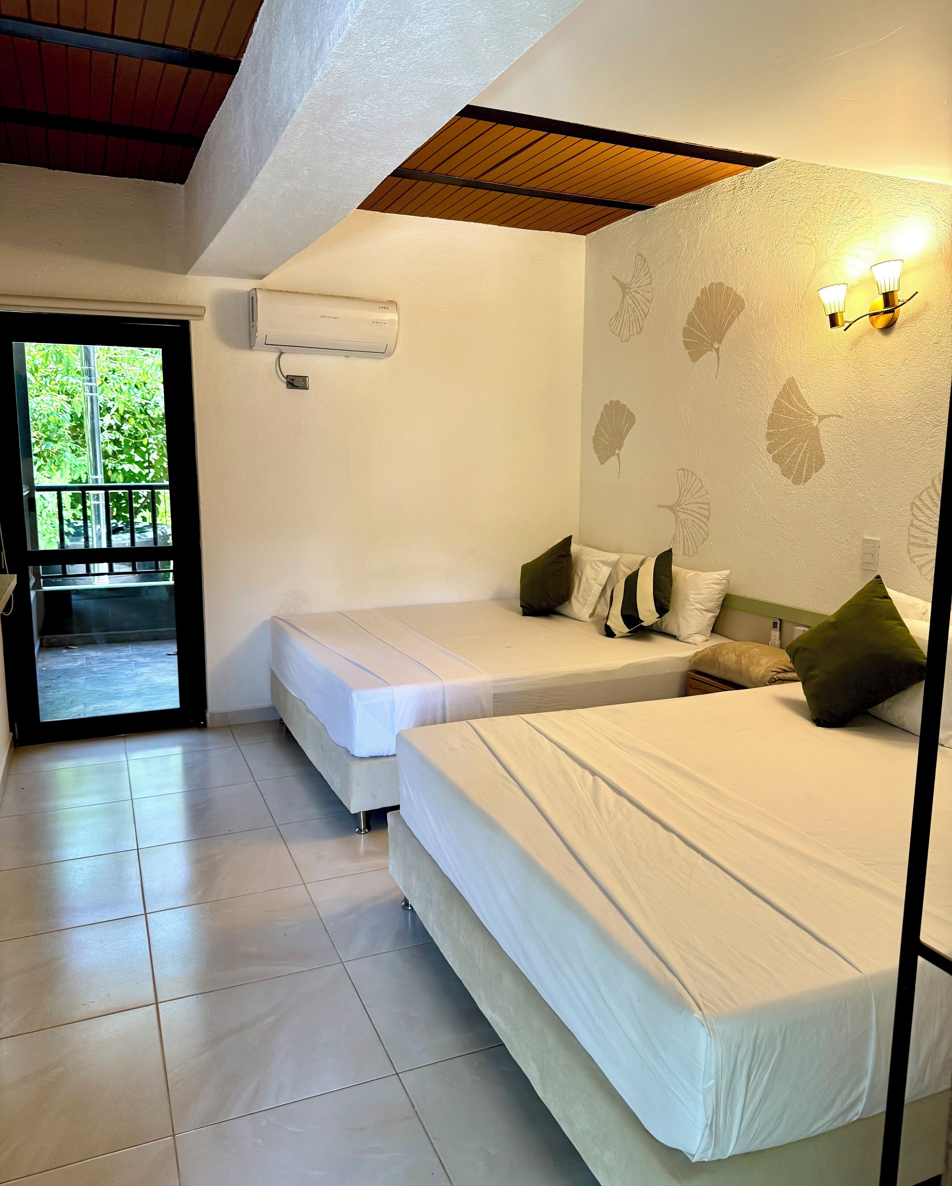 A hotel room with two beds, a balcony, and a wall-mounted air conditioner.