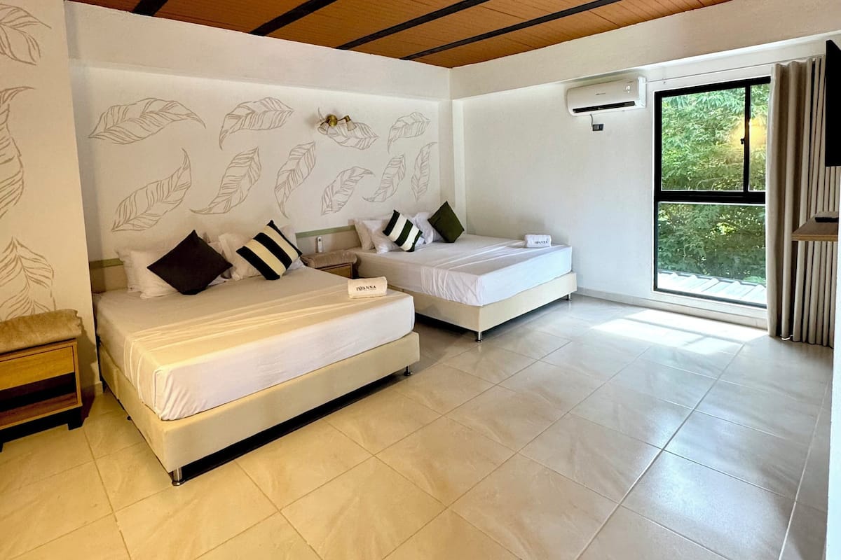 A spacious room with two beds, a large window, and a ceiling with exposed beams.