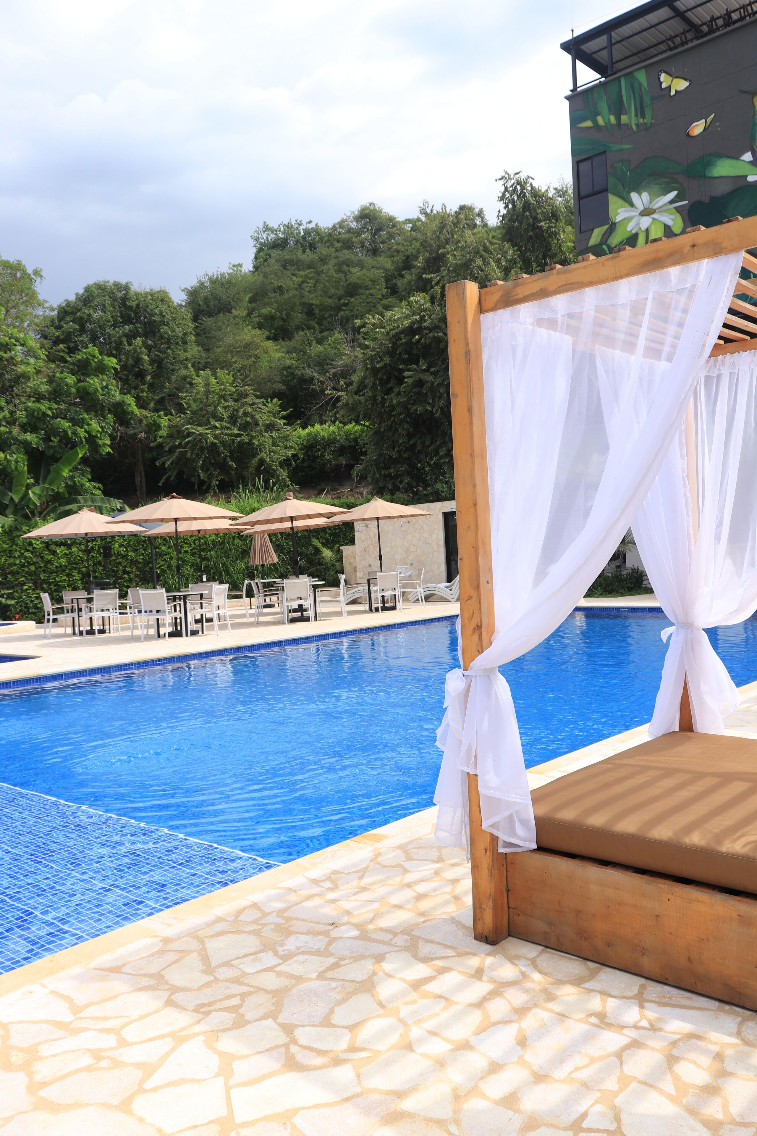A poolside area with a wooden bench, white canopies, and lounge chairs.