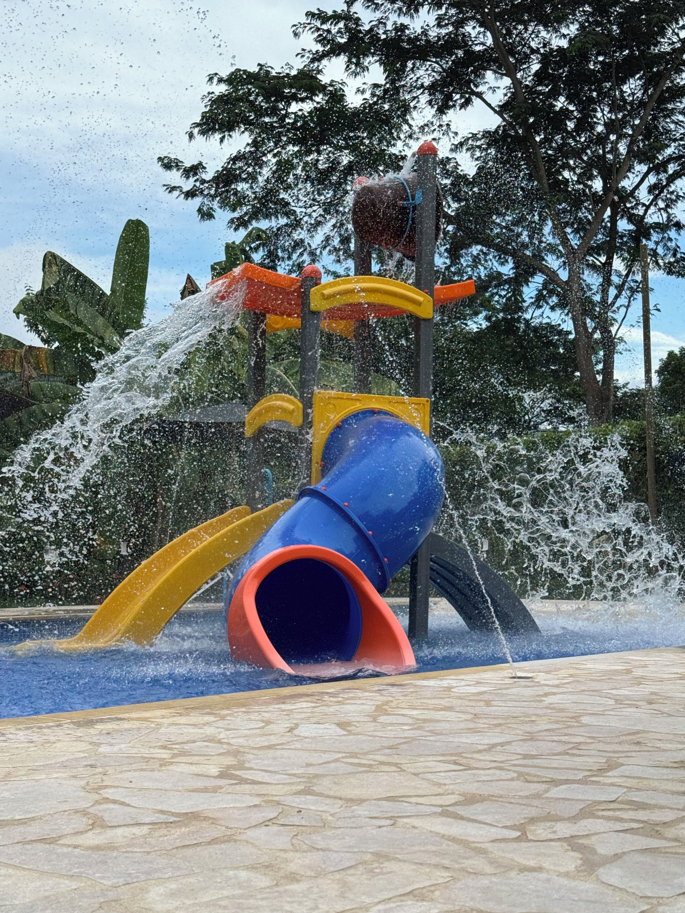 A water play area with a blue and yellow slide and a water fountain.