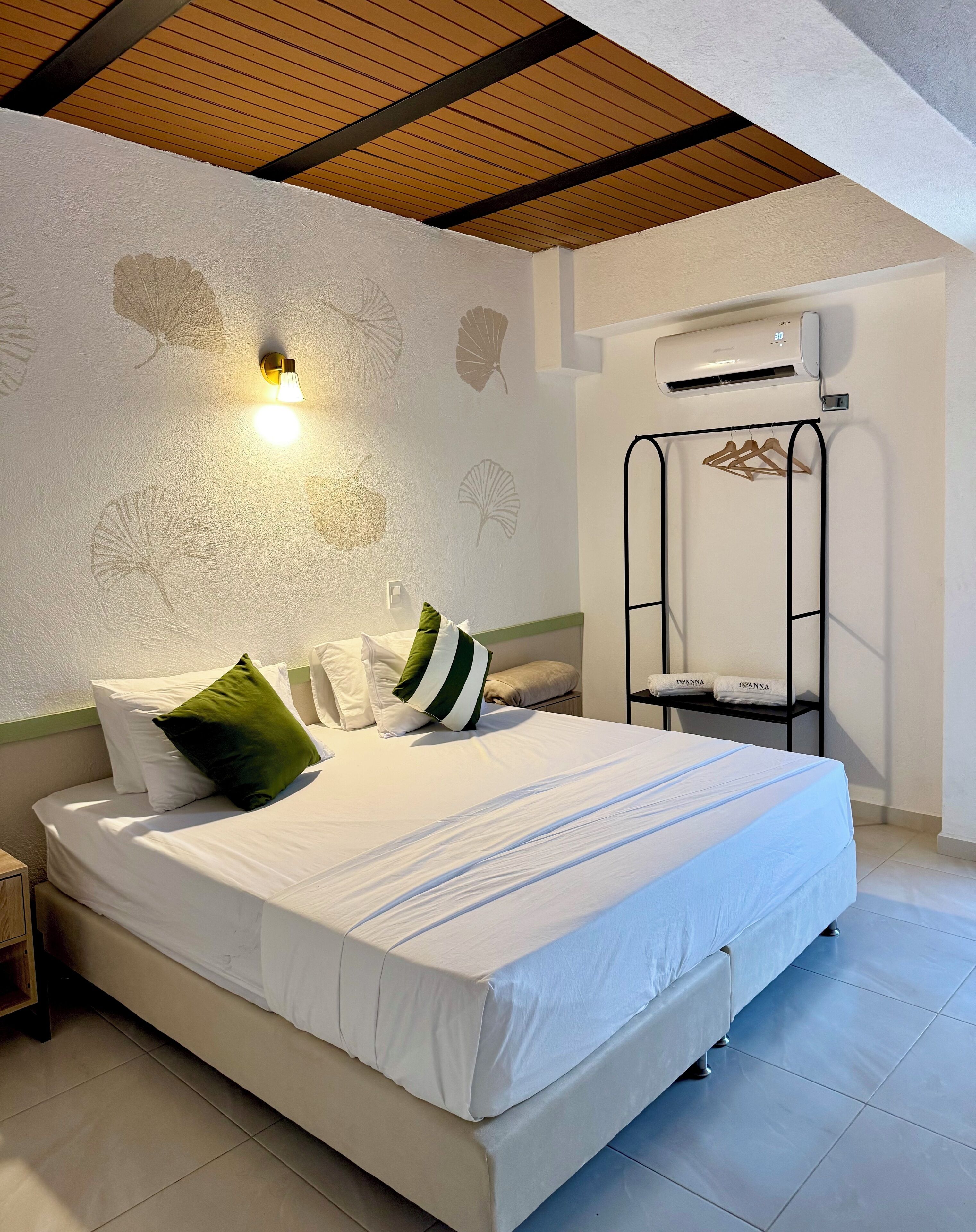A neatly made bed with white linens and green pillows, a wall-mounted light, and a ceiling fan.