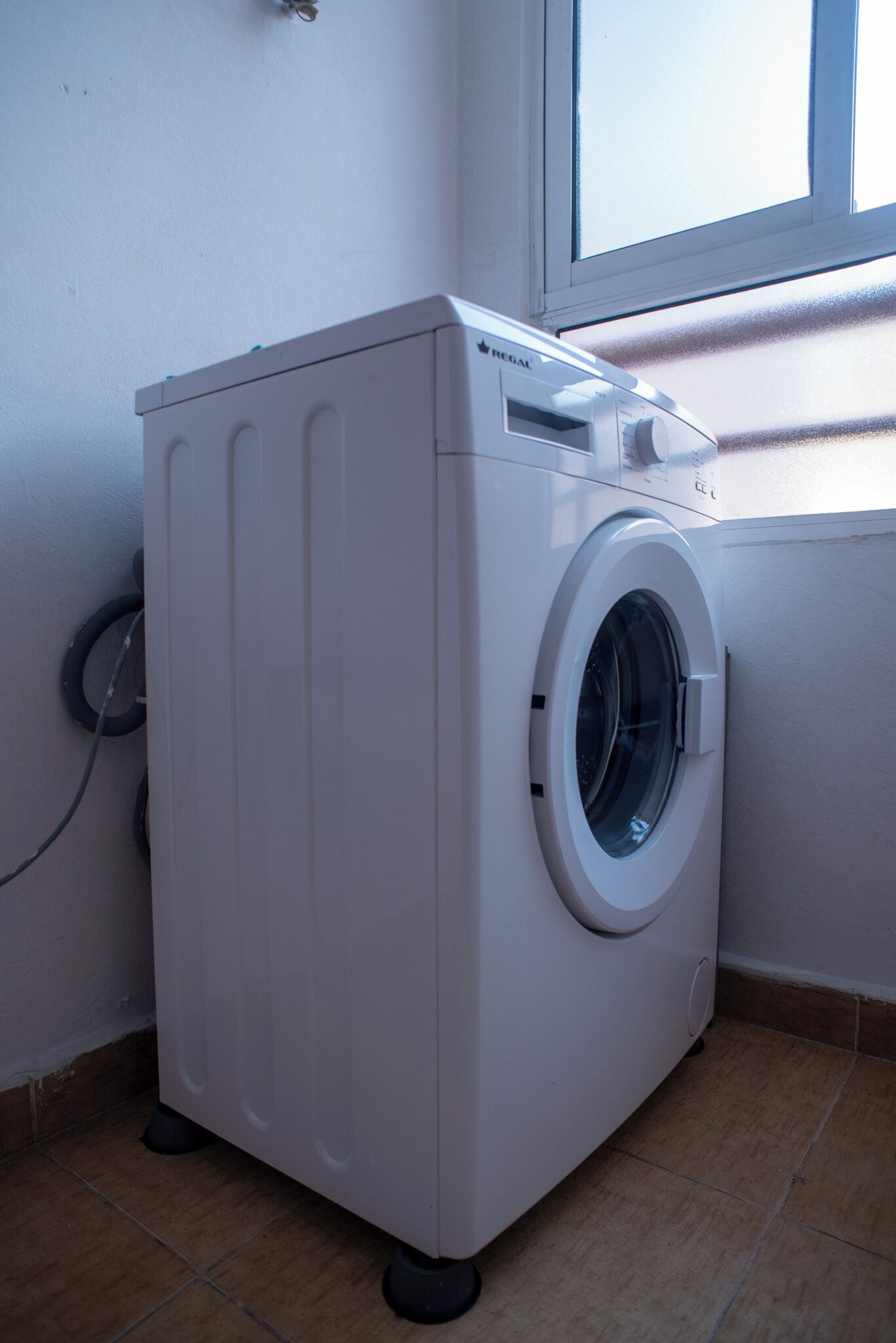 A front-loading washing machine in a corner with a window above it.