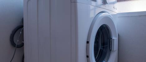 A front-loading washing machine in a corner with a window above it.