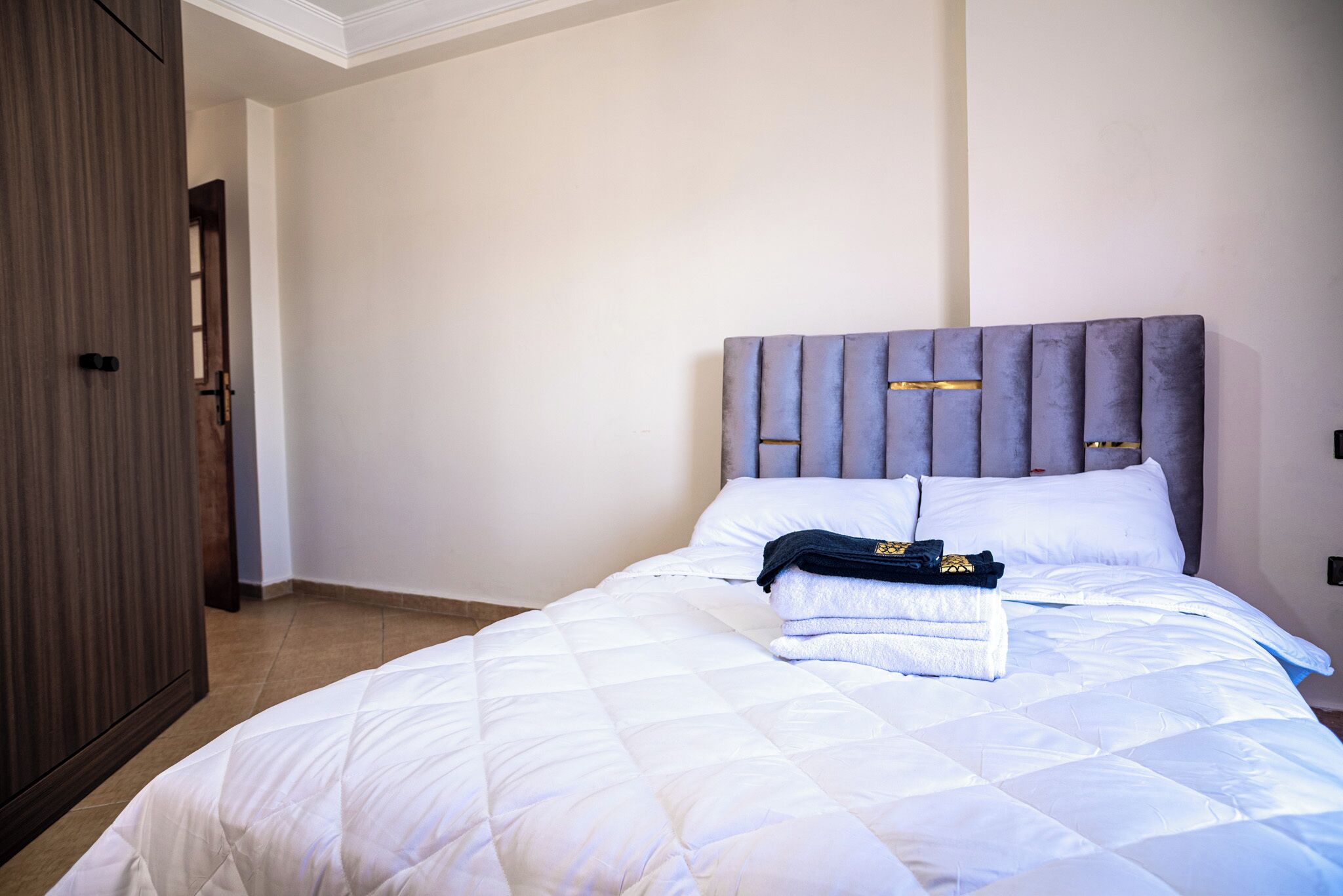 Una cama bien hecha con una colcha blanca acolchada y un cabecero tapizado en gris.