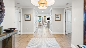 A hallway with a patterned rug, a chandelier, framed pictures, and a stone fireplace. - Portofino Island Resort 4-704 (Pensacola Beach)