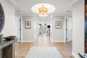 A hallway with a patterned rug, a chandelier, framed pictures, and a stone fireplace. - Portofino Island Resort 4-704 (Pensacola Beach)