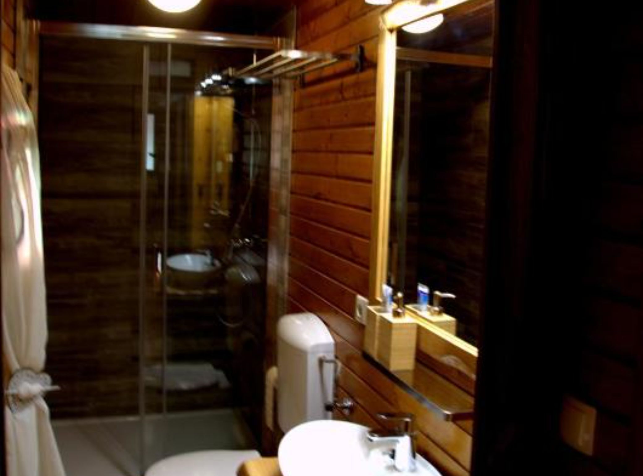 A wooden bathroom with a glass shower enclosure, a sink, and a mirror.