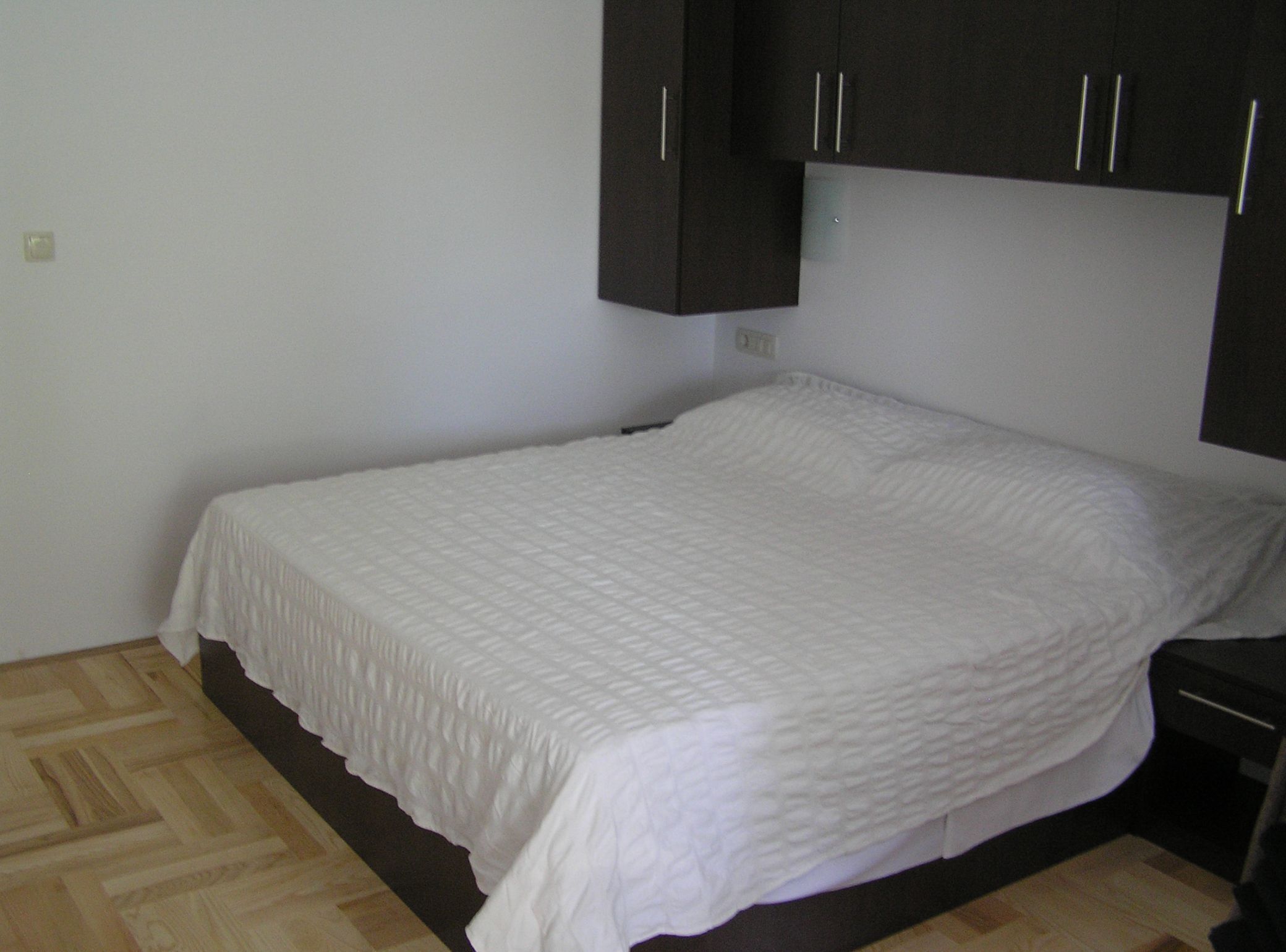 A single bed with a white quilt in a room with wooden flooring and dark cabinets.