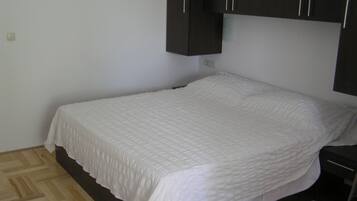 A single bed with a white quilt in a room with wooden flooring and dark cabinets.