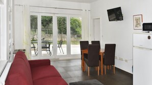 Un espacio habitable pequeño con un sofá rojo, una mesa de comedor con sillas, un televisor en la pared y un refrigerador.
