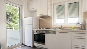 Una cocina moderna con armarios blancos, horno integrado, lavavajillas y una ventana con persianas.