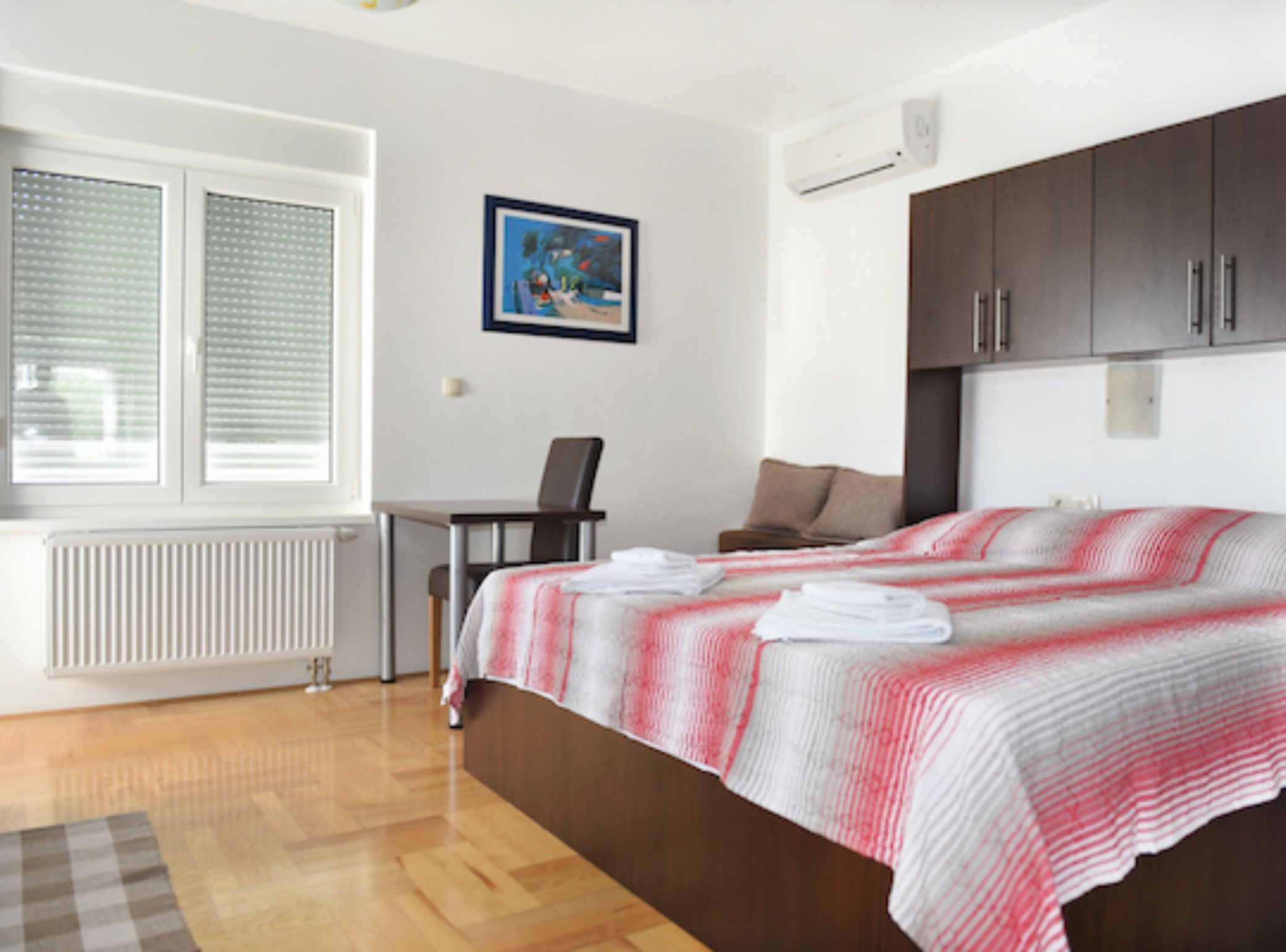 Un dormitorio con una cama, un escritorio, una silla, un radiador y una ventana con persianas.