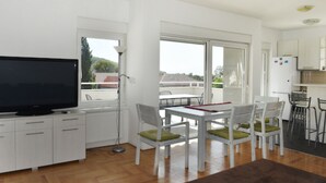 Una cocina moderna con armarios blancos, un comedor con sillas y mesa blancos, y un televisor de pantalla plana grande sobre un mueble.