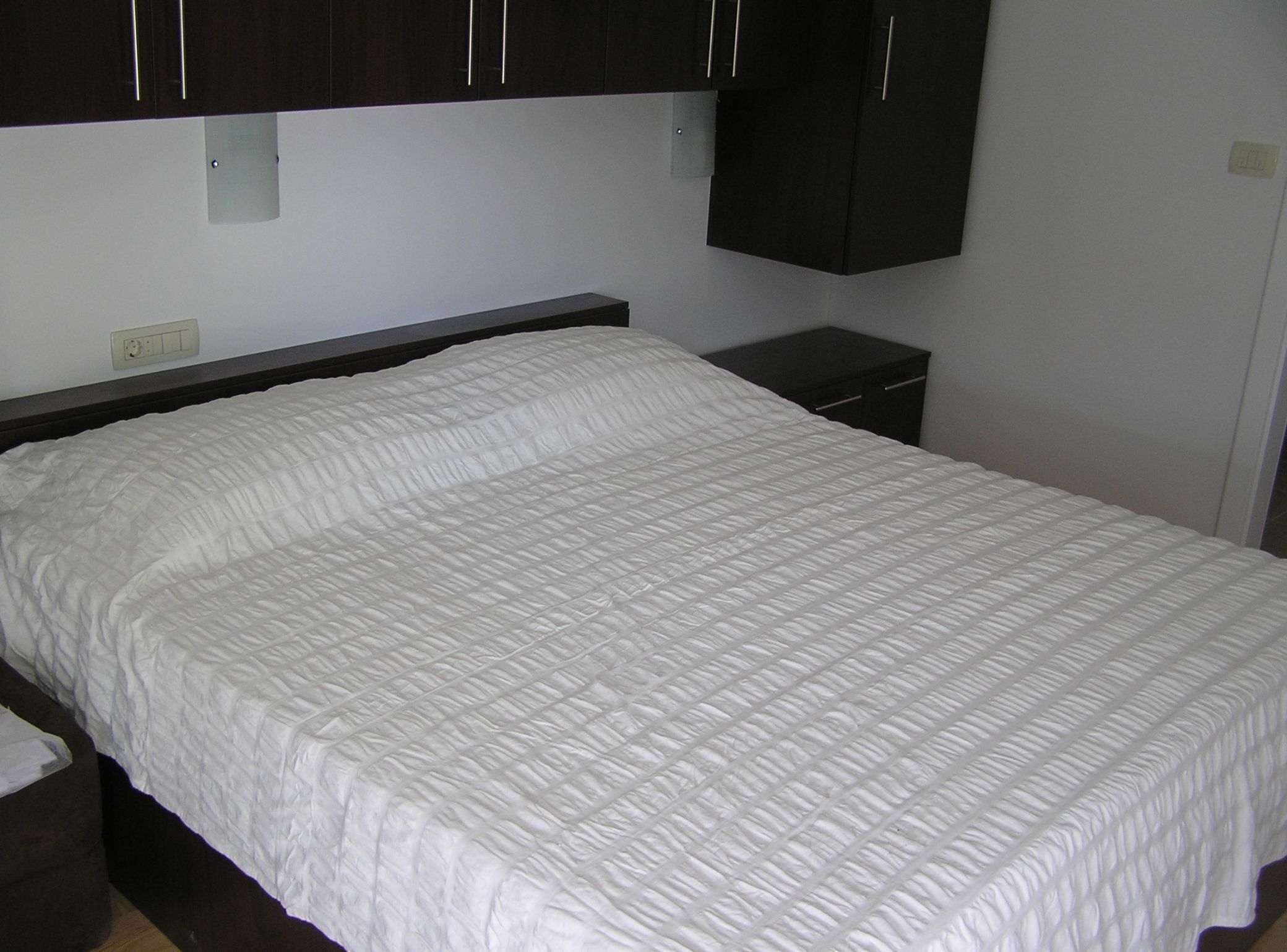 Una cama bien hecha con colcha blanca en una habitación con armarios de madera oscura.