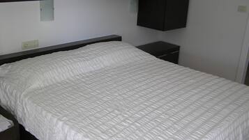 Una cama bien hecha con colcha blanca en una habitación con armarios de madera oscura.