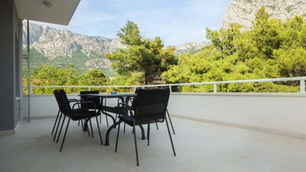Un balcón con una mesa y sillas, con vistas a un paisaje montañoso con árboles.