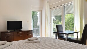 Habitación de hotel con cama, televisión, escritorio con silla y puerta corrediza de vidrio que da a un balcón.