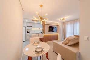 Ein modernes Wohnzimmer mit Essbereich, einer Couch, einem Fernseher und einer Küche im Hintergrund.