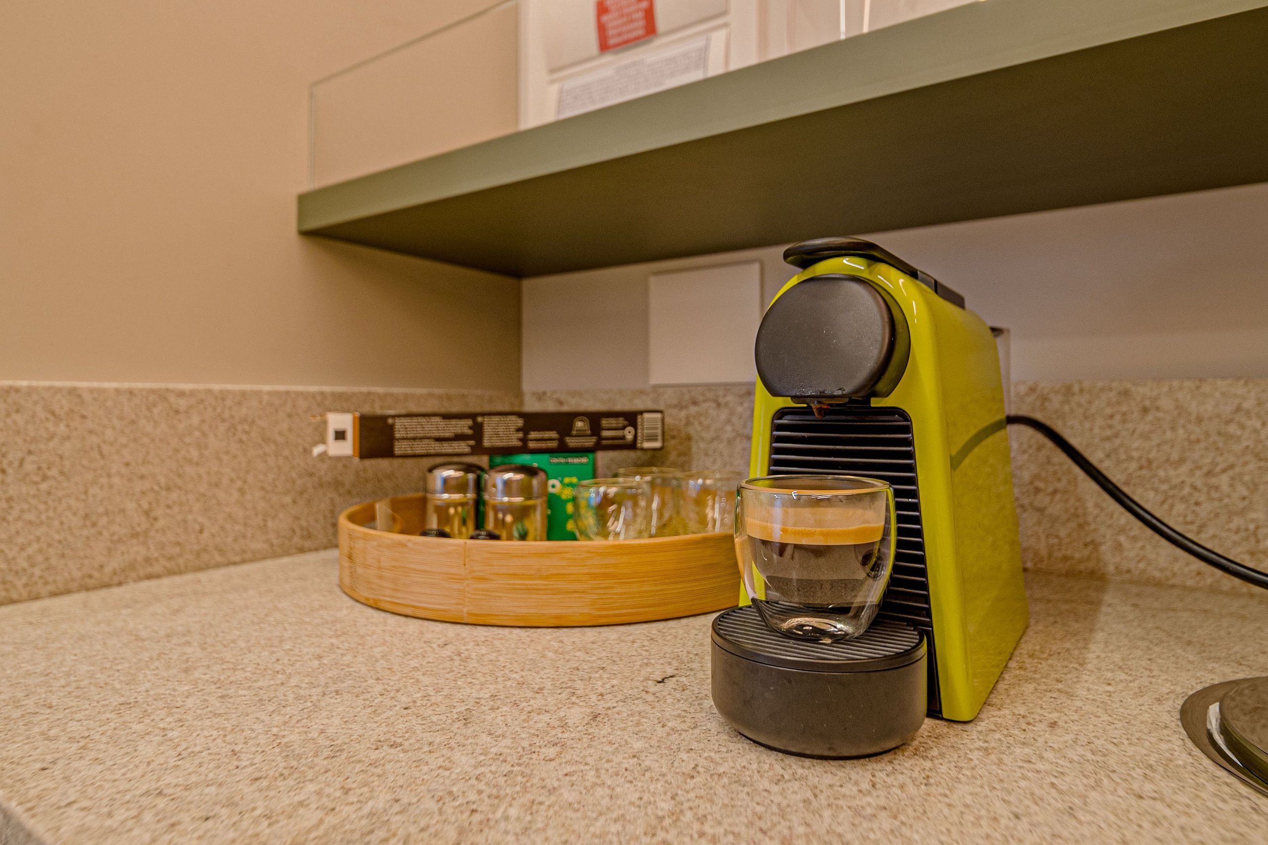 A coffee machine, a glass, and a bamboo tray on a kitchen counter.