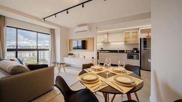 A modern living room with a sofa, dining table set for four, and a kitchen in the background.