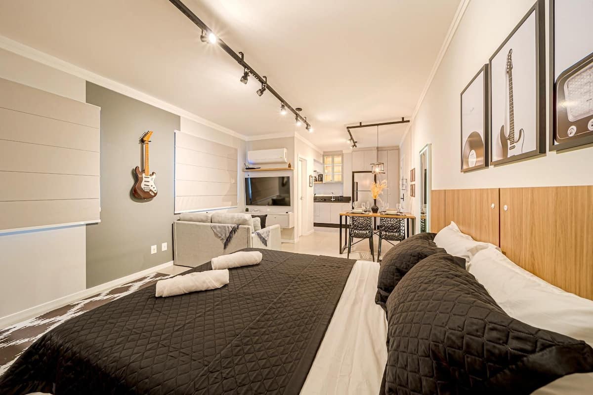 Une chambre d’hôtel moderne avec un grand lit, un bureau, une chaise, une télévision et des guitares encadrées accrochées au mur.