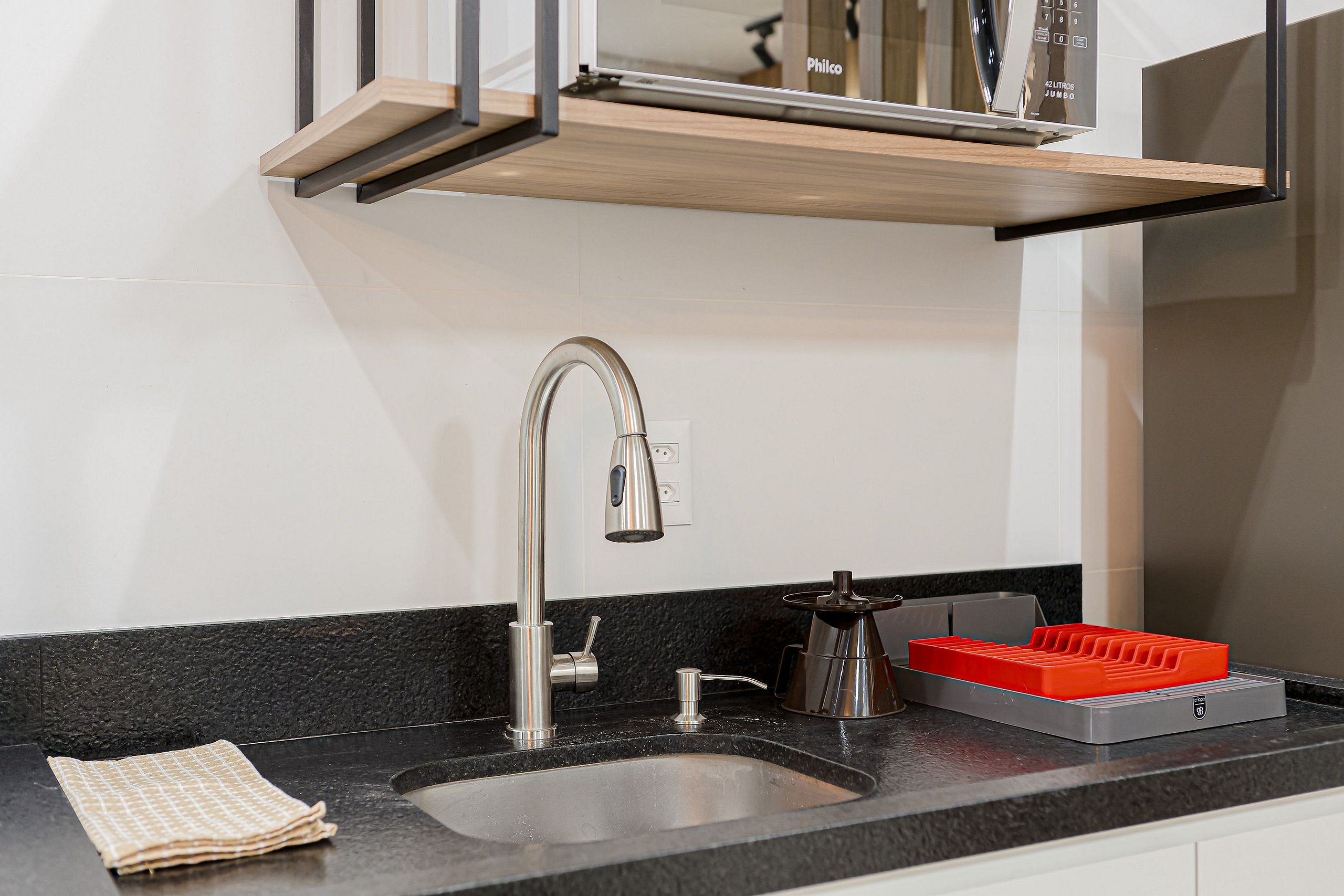Una cocina moderna con un lavamanos de acero inoxidable, un estante de madera encima y un electrodoméstico rojo sobre la encimera.
