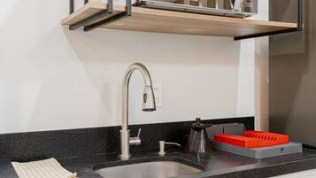 Una cocina moderna con un lavamanos de acero inoxidable, un estante de madera encima y un electrodoméstico rojo sobre la encimera.