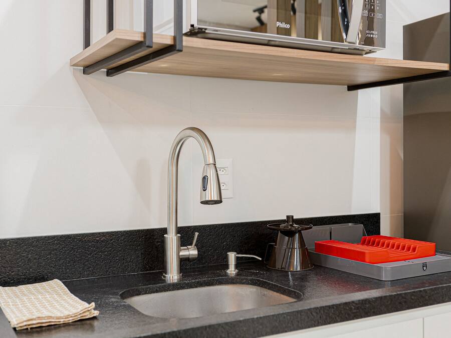 Una cocina moderna con un lavamanos de acero inoxidable, un estante de madera encima y un electrodoméstico rojo sobre la encimera.