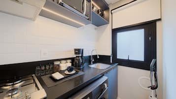 Una cocina compacta con estufa a gas, cafetera, pileta y ventana.