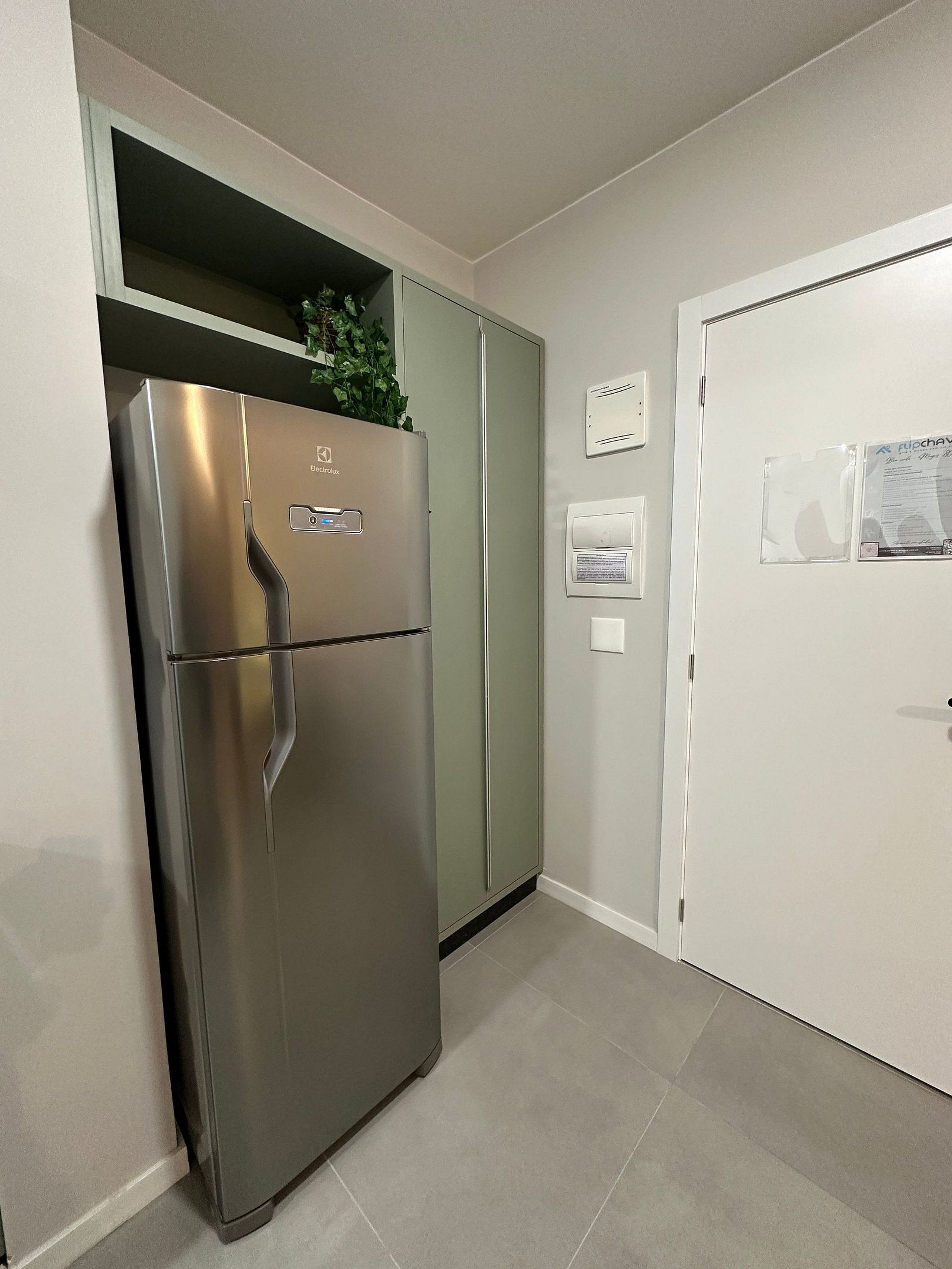 Un refrigerador de acero inoxidable con un panel de control, un gabinete verde, una puerta blanca con cerradura y un termostato fijado a la pared.