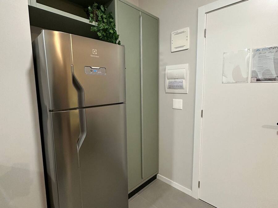 Un refrigerador de acero inoxidable con un panel de control, un gabinete verde, una puerta blanca con cerradura y un termostato fijado a la pared.