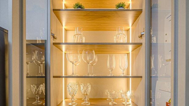 Een keuken met houten planken en glazen kasten, gevuld met keukengerei en servies.