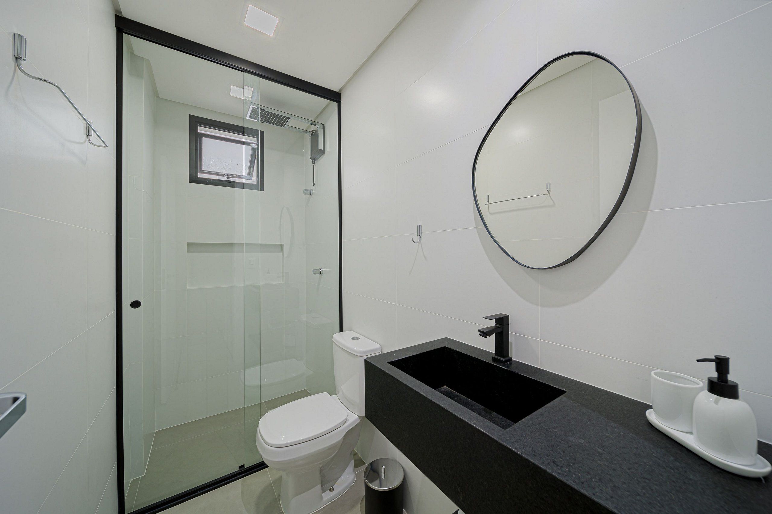 Un bagno moderno con box doccia in vetro, un water bianco, un lavandino nero con uno specchio sopra e un piccolo cestino.