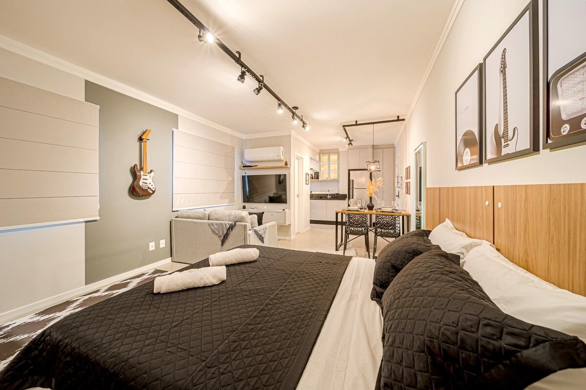 A modern hotel room with a large bed, a desk, a chair, a TV, and framed guitars on the wall.