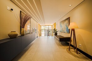 A modern hotel lobby with a long reception desk, a large painting, and a lamp. - Mingus Residencial Flipchave MIN000 (Joinville)