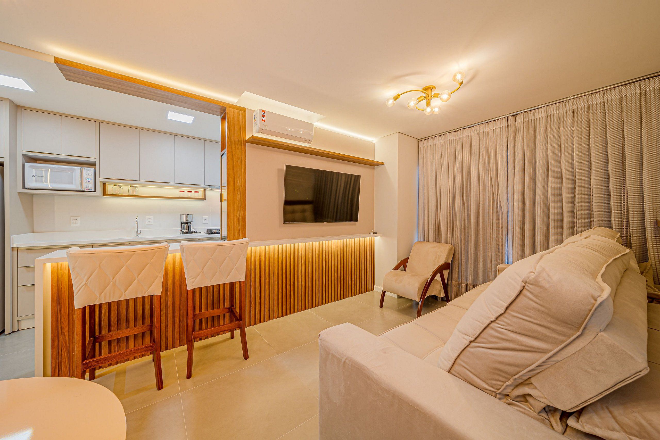 Una sala de estar moderna con un sofá, una zona de comedor con mesa y sillas, un televisor montado en la pared y un equipo de aire acondicionado.