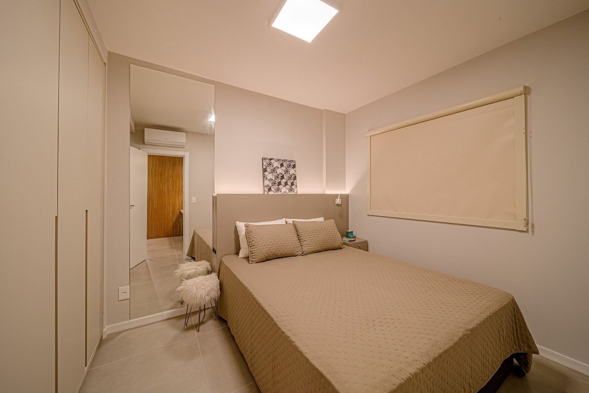 Une chambre à coucher comprenant un lit, une table de chevet, un miroir et une porte donnant sur une autre pièce.