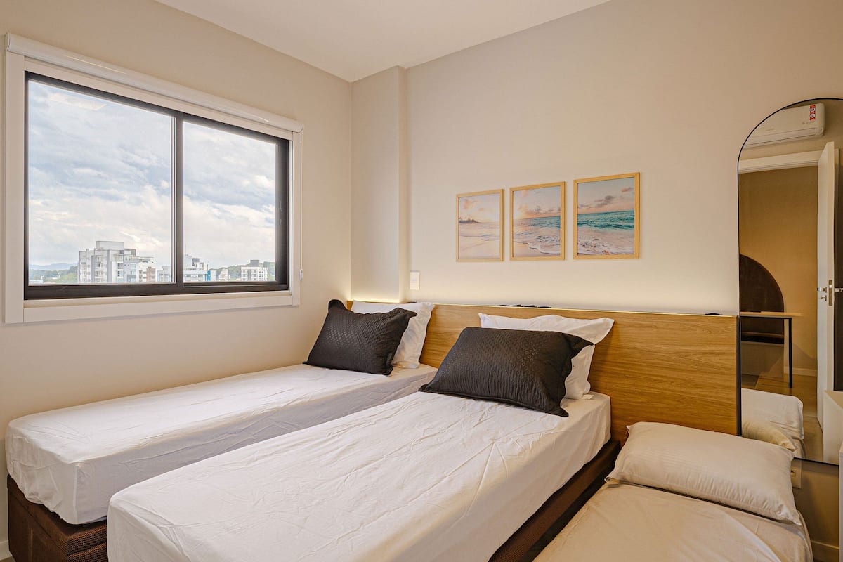 Une chambre d’hôtel avec deux lits, une grande fenêtre, une vue sur les immeubles et trois tableaux encadrés accrochés au mur.