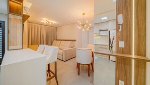 Een moderne hotelkamer met een zithoek, een bank, een stoel, een bureau en een keuken op de achtergrond.
